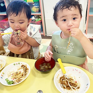 手やスプーンで麺を口に運ぶ子どもたち