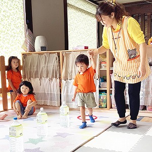 先生に手を引かれてペットボトルをよけてジグザグ歩く練習をする子ども