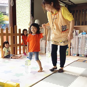 先生に手を引かれてペットボトルをよけてジグザグ歩く練習をする子ども