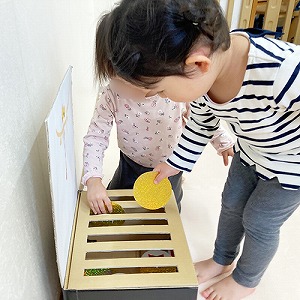 手作り賽銭箱にコインを入れながら中を覗き込む子ども