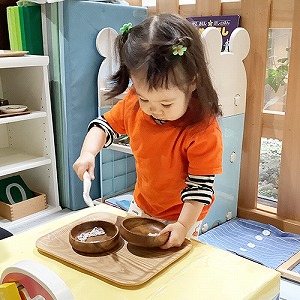 器の中身をスプーンで移す子ども