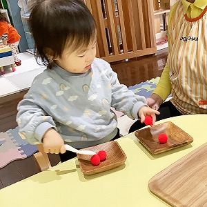 赤いボンボンを皿から皿へ移す子ども